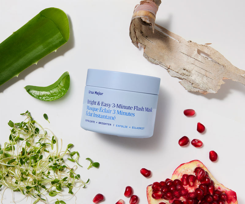 A light blue jar of Ultra Major Bright & Easy 3-Minute Flash Mask centered on a white background, styled with aloe vera, pomegranate seeds, sprouts, and dried bark.